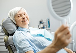 A senior woman admiring her new implant dentures in a hand mirror