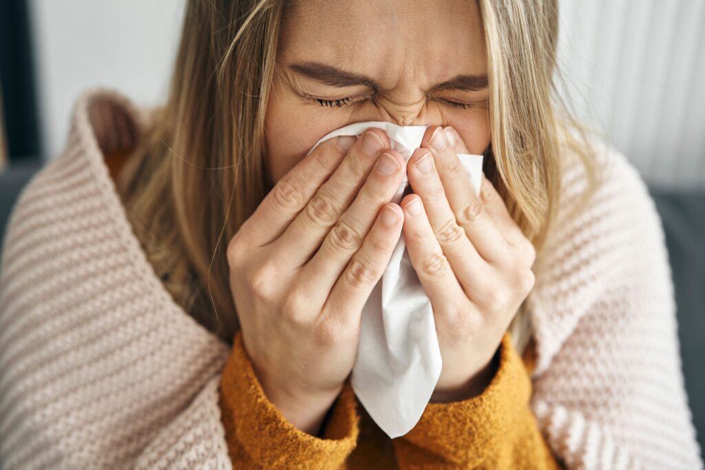 Woman with blond/brown hair wrapped in blanket blowing her nose